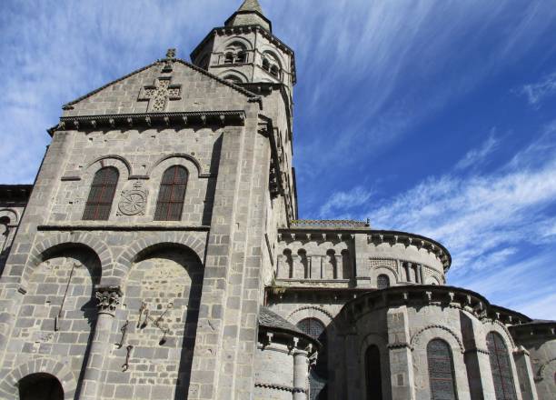 Volcanic stone religious building Horizontal sunny view against the dive of the Basilica of Notre Dame d'Orcival. Background of blue sky hatched with white clouds. Auvergne-Rhône-Alpes, France. August 2020. orcival stock pictures, royalty-free photos & images