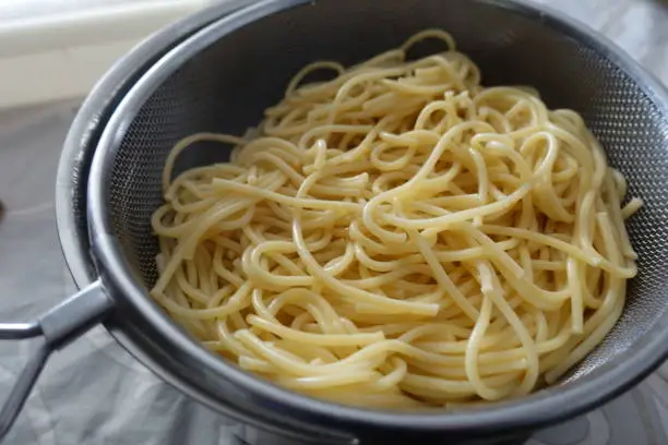 Spaghetti cooked in water put in a colander to drain