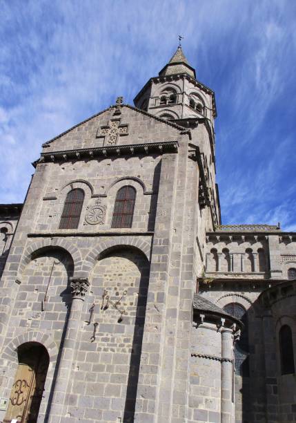 Volcanic stone religious building Sunny vertical view against the dive of the Basilica of Notre Dame d'Orcival. Background of blue sky hatched with white clouds. Auvergne-Rhône-Alpes, France. August 2020. orcival stock pictures, royalty-free photos & images