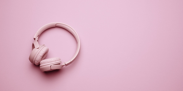 pink wireless headphones on a pink background, banner. Top view on modern gadget, place for an inscription
