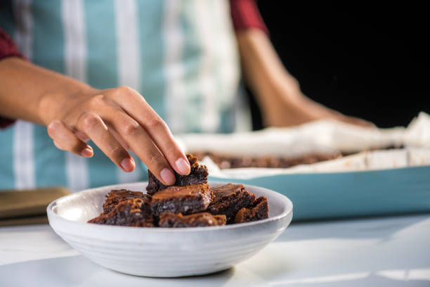 Close-up of female hand serving chocolate brownie in plate.