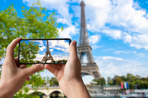 Tourist taking photo of Eiffel tower in Paris, France. Man holding phone and taking picture.