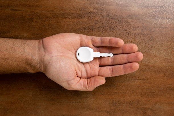 dans la main de l’homme est une clé blanche d’une vieille voiture. ci-dessous est une base en bois brun. - human hand key giving carrying photos et images de collection