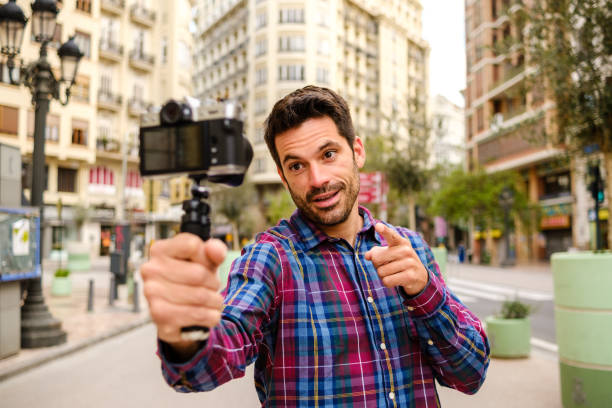 Young Latino adult man records a video with a camera in a city stock photo