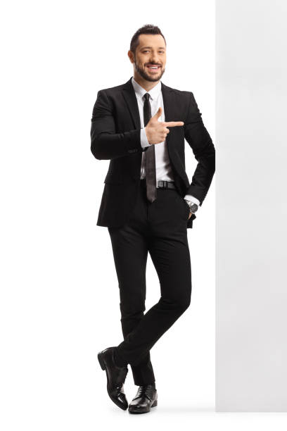istock Professional man in a suit and tie leaning on a wall and pointing to the side 1313628594