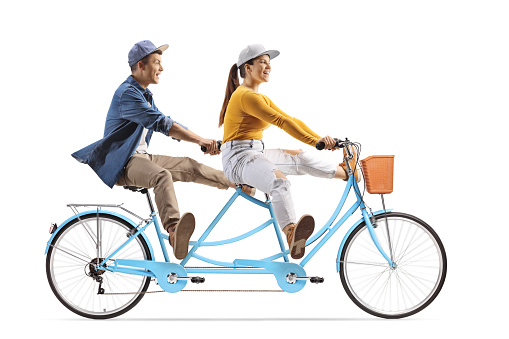 Full length profile shot of a young male and female riding a tandem bicycle and lifitng legs isolated on white background