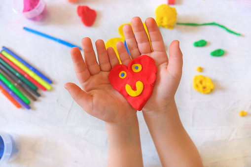 Child playing with plasticine, colorful modeling clay and sculpting heart . Home Education game with clay. Early development . Handmade concept for birthday, mothers day or valentines day