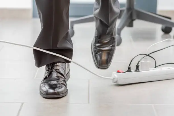 Close up of a businessman legs stumbling with an electrical cord at office