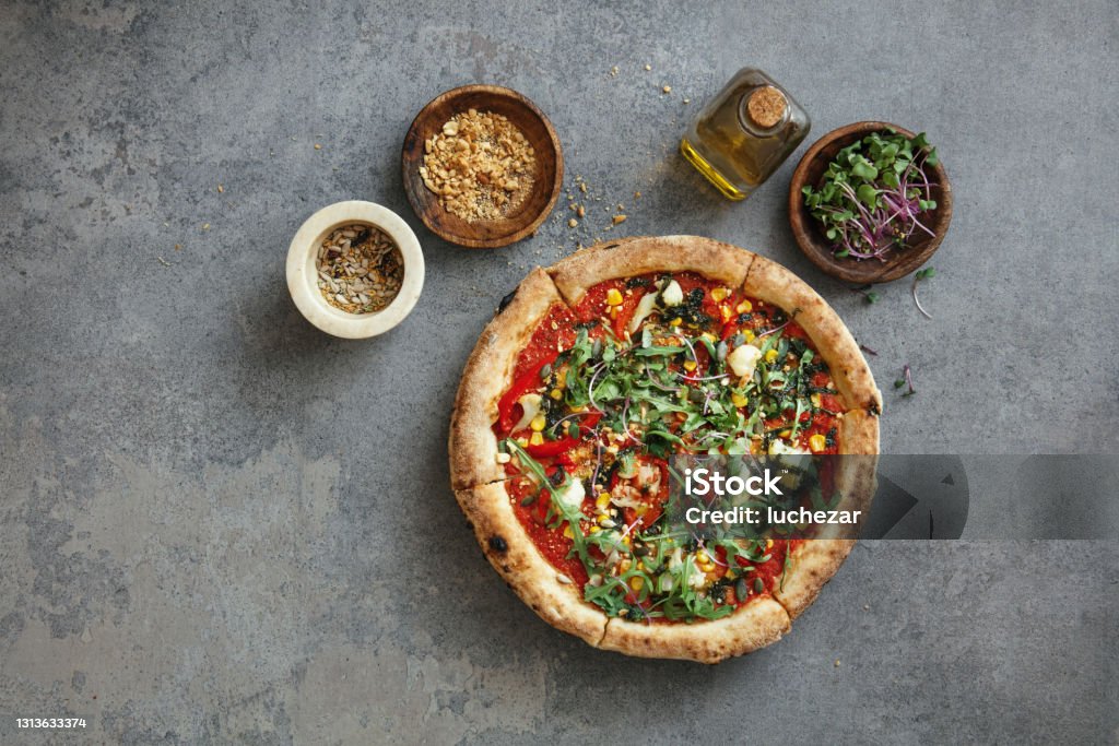 Vegatarian Pizza Vegetarian pizza with tomato sauce, cauliflower, corn, arugula, nuts and microgreen. Flat lay top-down composition on concrete background. Vegetarian Pizza Stock Photo