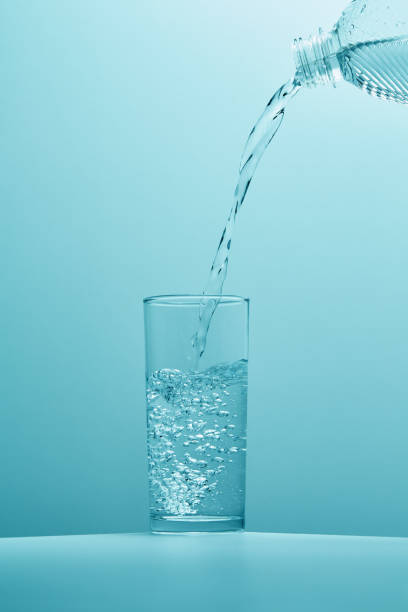 pouring clear drinking water from a bottle in to a clear glass creating bubbles - water water bottle glass pouring imagens e fotografias de stock