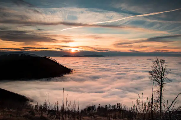 Photo of last rays of the sun cross the clouds and go behind a high mountain and put the earth in the dark. View from Ondrejnik mountain, Czech Republic. Being above the clouds