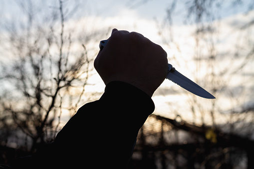 A knife in the hand of a man with a sharp steel blade in the park as a weapon or a means of self-defense.