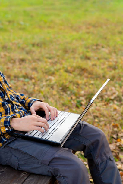 man sits in park and works at laptop outdoors. hands typing on keyboard - surfing wireless vertical outdoors lifestyles imagens e fotografias de stock