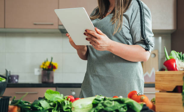 istock Unrecognizable woman reading recipe on digital tablet while cooking lunch in modern kitchen 1313643255