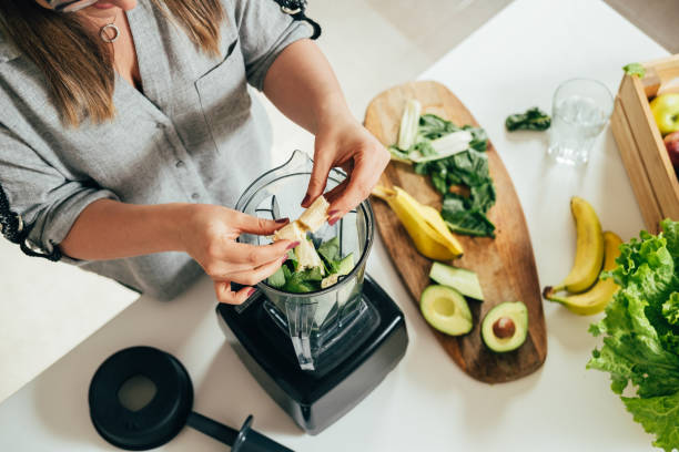 la donna sta preparando una bevanda detox sana in un frullatore - un frullato verde con frutta fresca, spinaci verdi e avocado - disintossicazione foto e immagini stock