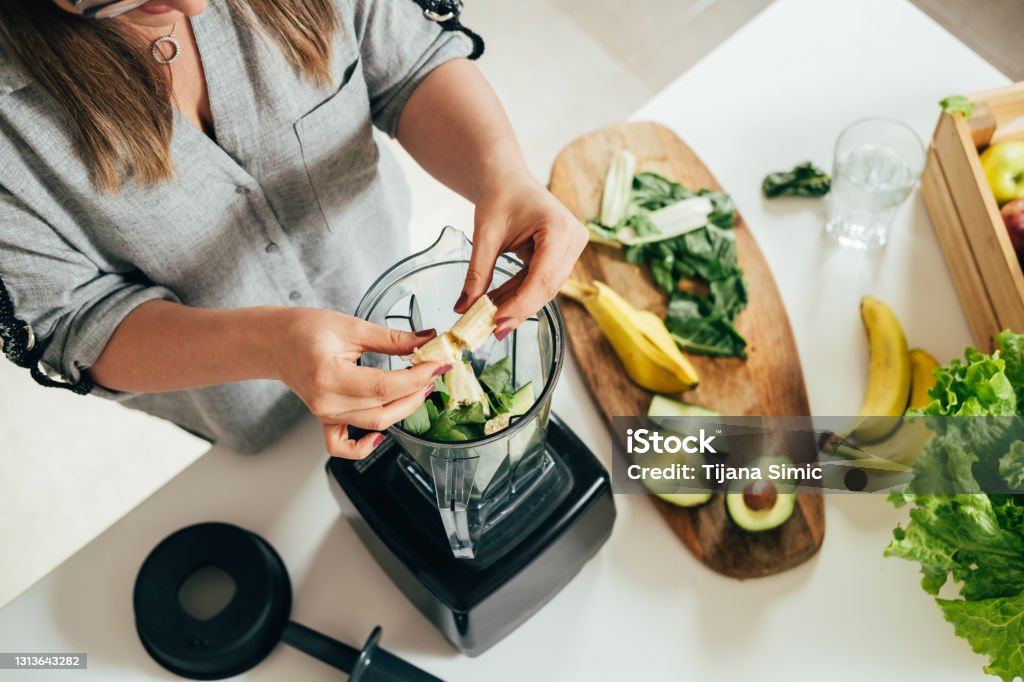 Woman is preparing a healthy detox drink in a blender - a  green smoothie with fresh fruits, green spinach and avocado Healthy eating concept, ingredients for smoothies on the table, top view Healthy Eating Stock Photo