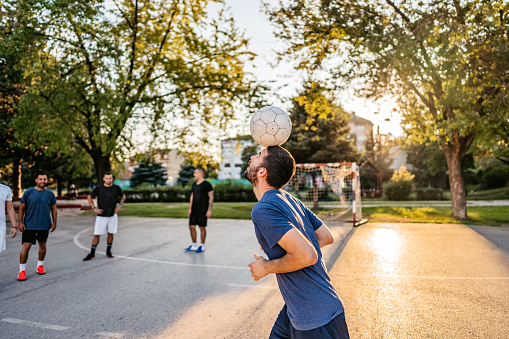 Man is juggling soccer ball with his head of urban soccer field.
