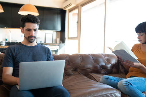 Portrait of young couple spending time together sitting on couch while staying at home. New normal lifestyle concept.