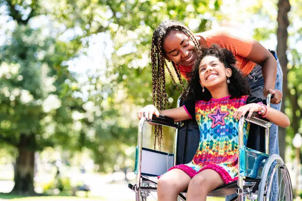 Photo of Little girl in a wheelchair at the park with her mother.