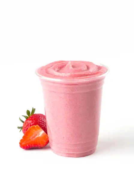 Strawberry smoothie in a disposable cup with fresh strawberries on the side.
