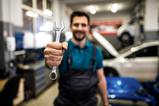 Young car mechanic holding a wrench, Close- up photo and focus on a tool. Repairman ready for work.
