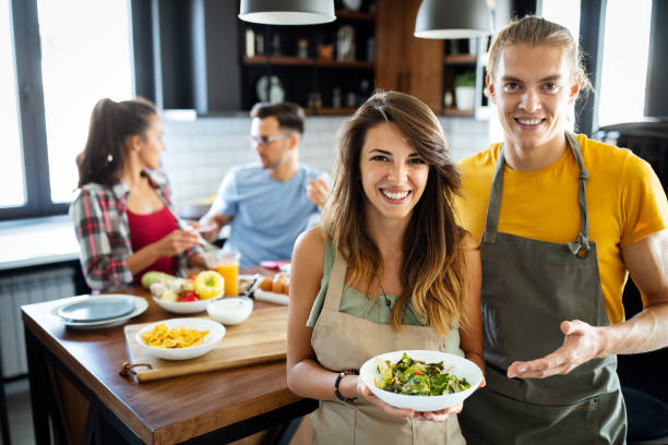 group of happy friends laughing and talking while preparing meals in kitchen - gourmet enjoyment food freshness imagens e fotografias de stock