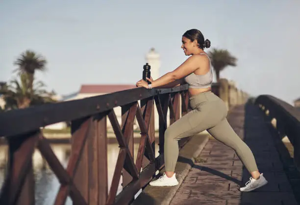 Photo of Shot of a young woman stretching on a footbridge