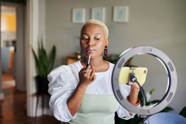 Young African influencer putting on lip gloss during a vlogcast