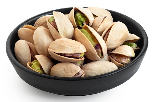 Salted pistachios in shell in a black ceramic bowl isolated on white.