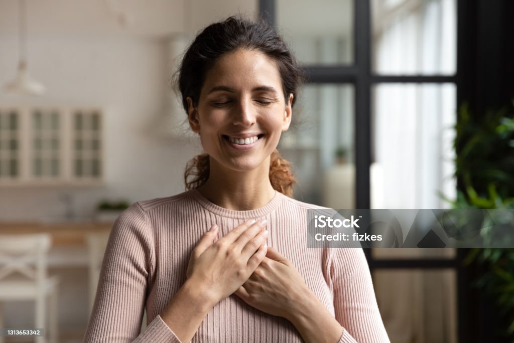 Peaceful hispanic female with closed eyes keep hands to heart Thank you my God. Happy peaceful millennial hispanic lady stand alone with closed eyes keep hands close to heart hope pray in mind. Emotional young woman express deep gratitude impressed by good deed Gratitude Stock Photo