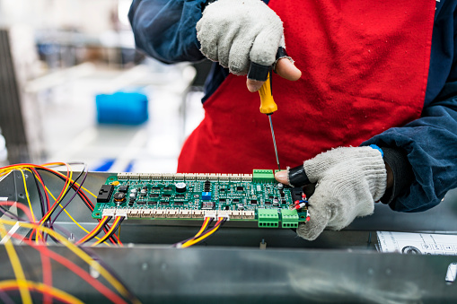 Professional young industrial factory woman employee working with machine parts putting, checking and testing industrial equipments cables in large Electric electronics wire and cable manufacturing plant factory warehouse.