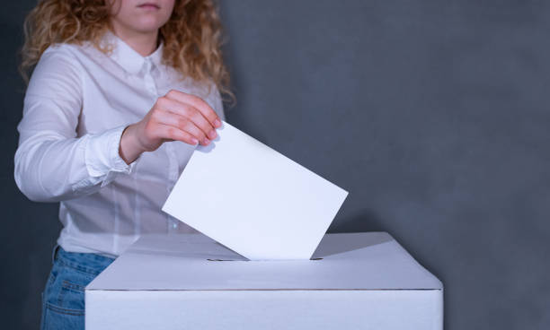 Young woman with curly hair in a white shirt stands behind a voting box and throws her ballot into it. Federal election Germany. german federal elections photos stock pictures, royalty-free photos & images