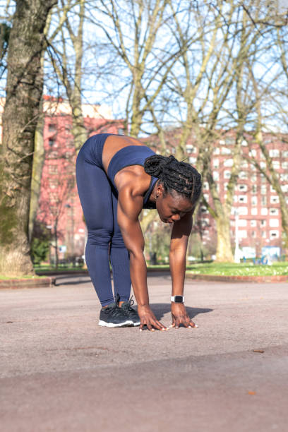 istock Black African woman warming up and doing back and leg stretches bending down to start doing sports in a public street park on a sunny day 1313658932
