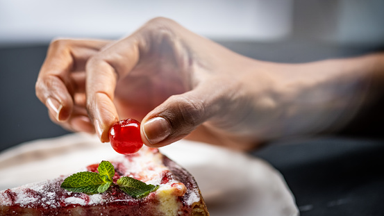 Close-up of woman's hand placing cherry on slice of cake.
