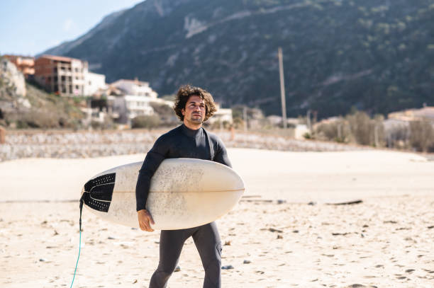 istock Young surfer man holding a surfboard and walking looking at distance. 1313666696