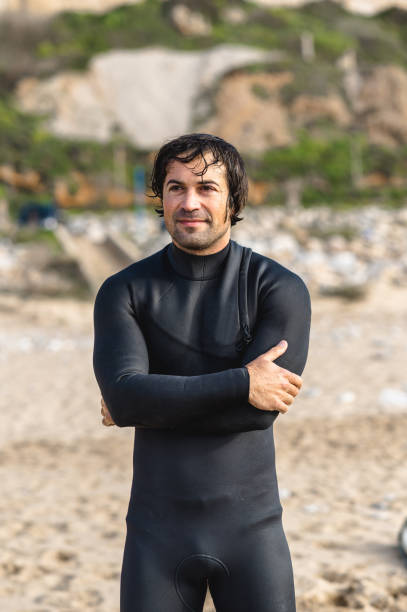 istock Vertical Medium shot young wet man wearing diving suit standing on the beach looking ahead with smiley face 1313666823