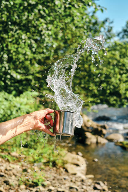 A splash of fresh water from a mug in the hands of a girl on the background of nature. Drinking water concept. A splash of freshness. Natural water. Healthy lifestyle. Cold water from a mountain river A splash of fresh water from a mug in the hands of a girl on the background of nature. Drinking water concept. A splash of freshness. Natural water. Healthy lifestyle. Cold water from a mountain river splash mountain stock pictures, royalty-free photos & images
