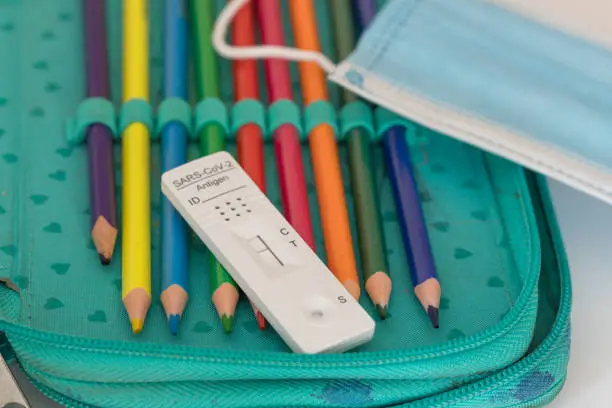 Surgical mask and Corona Sars-CoV-2 Antigen test with negative result on colored pencil in a pencil case, focus on foreground