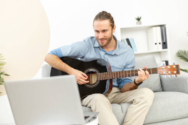 istock Concentrated young man at home with laptop playing guitar 1313677389