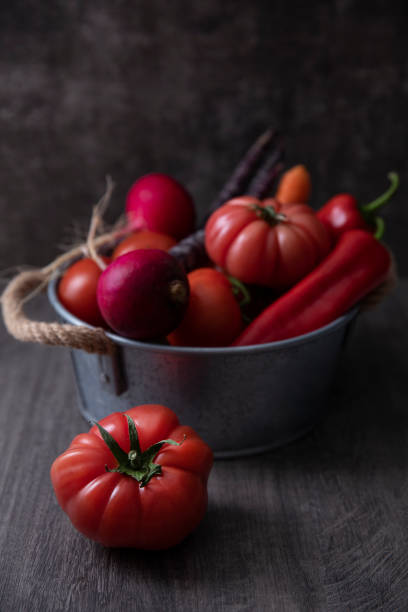 Fresh tomatoes, red peppers, carrots, and radish in a basket on dark wooden background