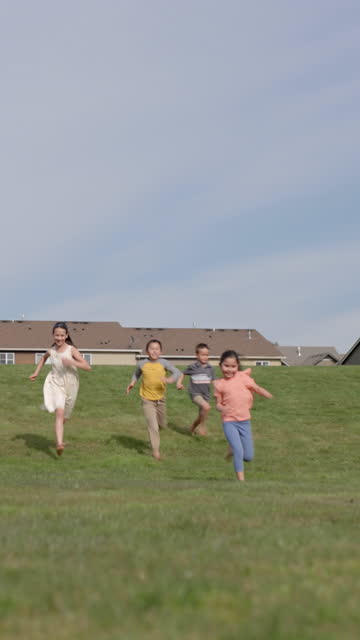 A multi-ethnic group of happy and playful elementary age children race down a hill while playing together outdoors in the sunshine on a warm day. The healthy group of kids are barefoot and wearing casual clothing. They are having fun in grassy park in a suburban neighborhood.