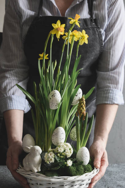 Easter floral composition for table centerpiece with yellow narcissus, festive eggs, moss and bunny.