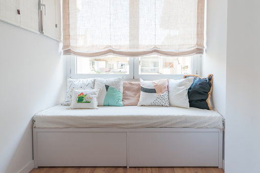 Sofa with many cushions close to the window in a bedroom.