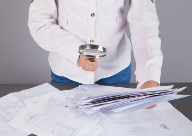 istock Businesswoman examines office documents with a mgnifying glass. 1313687971