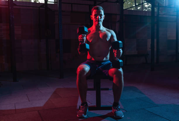 istock Muscular man exercise with dumbbells in red-blue gradient light in dark gym hall 1313692765
