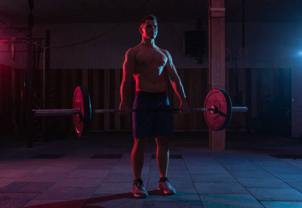 istock Working out by lifting weights in a cross-training gym. Muscular powerful man doing deadlift with a heavy barbell in red blue neon light 1313692781