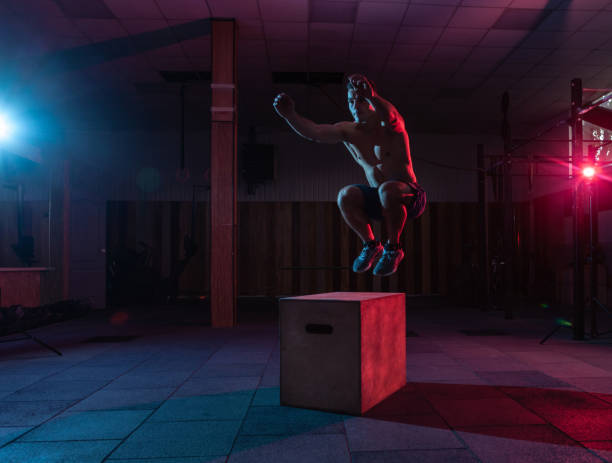 Muscular man trains jumping on a wooden box in a dark gym. Athlete Workout in red blue neon light. Cross, functional training Muscular man trains jumping on a wooden box in a dark gym. Athlete Workout in red blue neon light. Cross, functional training cross training stock pictures, royalty-free photos & images