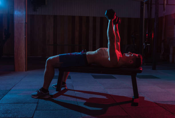 istock Muscular powerful man training bench press with dumbbells exercise in red blue neon light 1313692798