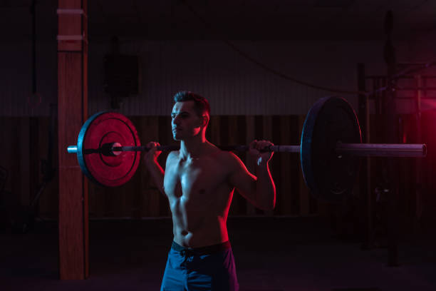 istock Working out by lifting weights in a cross-training gym. Muscular powerful man with heavy barbell in red blue neon light 1313692801