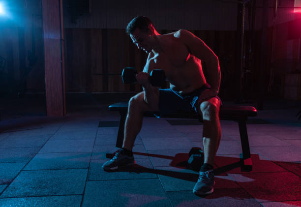 istock Muscular man training biceps, exercise with dumbbell in red-blue gradient light in dark gym hall 1313692826